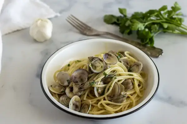 Un piatto invitante di linguine alle vongole, con aglio e prezzemolo freschi sullo sfondo.