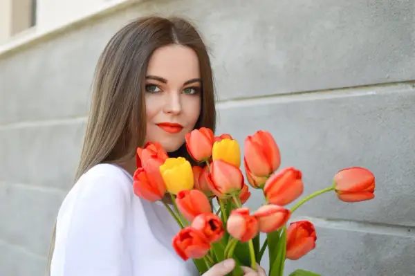 Uśmiechnięta dziewczyna z bukietem pomarańczowych i żółtych tulipanów, idealny prezent na imieniny Anity.