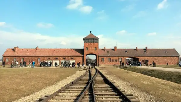 Brama obozowa Auschwitz I z wieżą, tory kolejowe prowadzące do niej. Zwiedzający zastanawiają się, ile trwa zwiedzanie Auschwitz, by poznać historię.