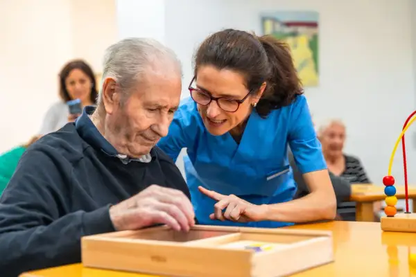 Un homme âgé participe à un atelier sensoriel, guidé par une aide-soignante attentive.