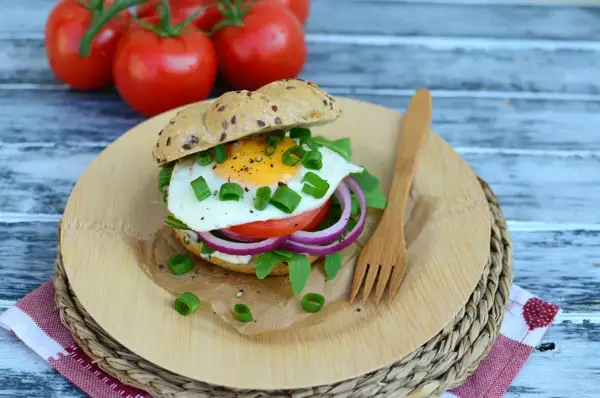 Pyszny burger z jajkiem sadzonym, rukolą, pomidorem i czerwoną cebulą na desce z drewna.