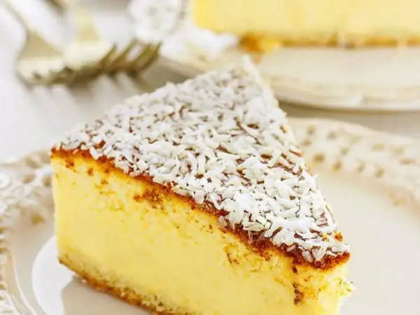 Una fetta di torta alla ricotta veloce e morbidissima, cosparsa di cocco grattugiato, su un piatto bianco.