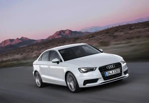 Białe Audi A3 jedzie po drodze w górach. Jego lekka konstrukcja i dynamiczny wygląd podkreślają jego sportowy charakter.