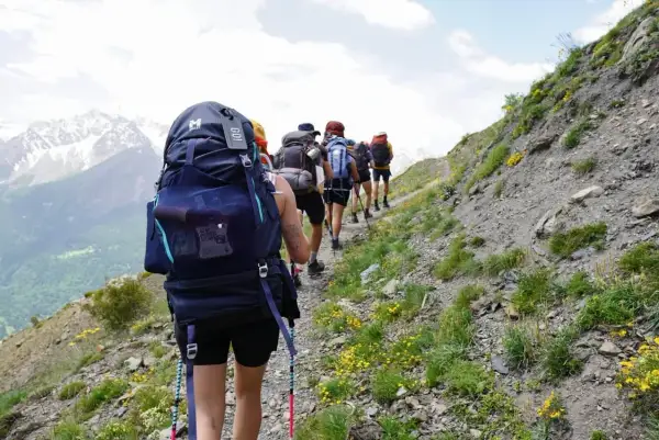 Groupe de randonneurs avec de gros sacs à dos sur un sentier de montagne. Le mot "GO!" est visible sur un sac.