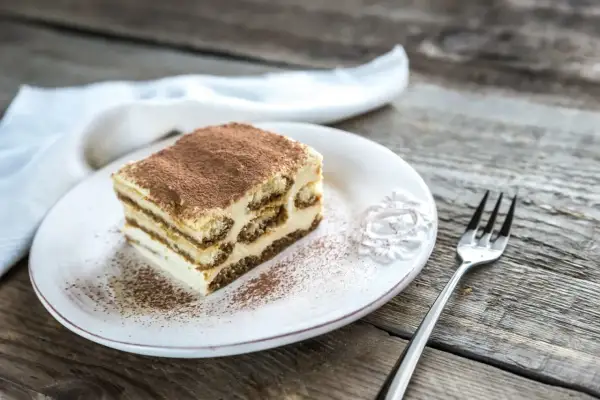 Une part de tiramisu maison, saupoudrée de cacao, sur une assiette blanche, prête à être dégustée. La conservation de ce délice est essentielle.