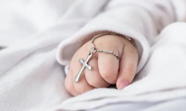 Dziecięca dłoń z krzyżykiem na bransoletce, symbol błogosławieństwa. Planujesz jak zorganizować chrzciny?