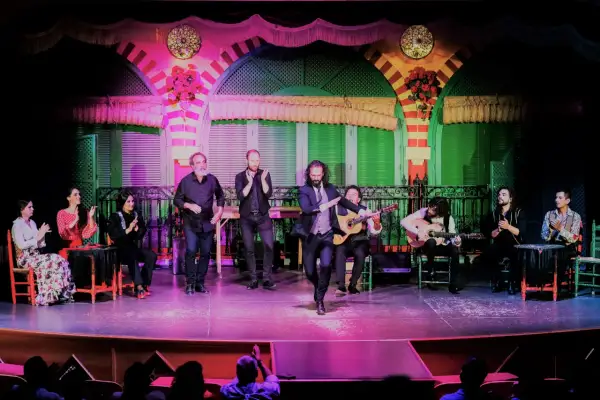 Un cantante sevillano flamenco baila en el escenario, acompañado por guitarristas y palmeros.