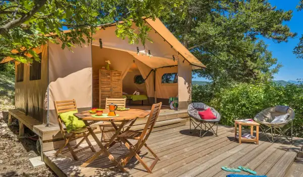 Tente aménagée pour un séjour insolite dans la Drôme, avec terrasse en bois, mobilier de jardin et vue sur la nature.