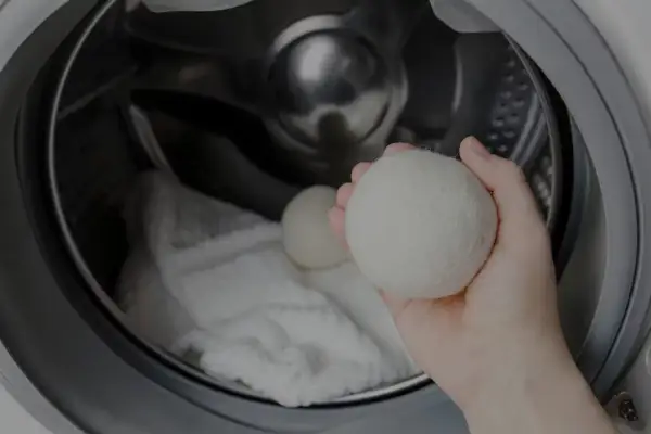 Mano che tiene una pallina per lavatrice, pronta per essere inserita nel cestello con il bucato. Scopri come si usa per un bucato più morbido.