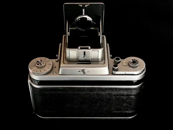 A vintage Pentacon Six camera, with its viewfinder open, sits on a reflective black surface.