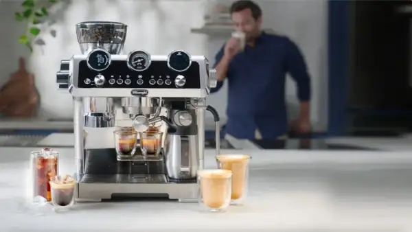 Macchina per caffè De'Longhi in azione, con chicchi pronti per la produzione del caffè. Un uomo assapora una bevanda calda.