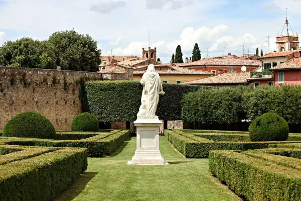 Statua bianca al centro degli Horti Leonini, con siepi geometriche e un muro di pietra.