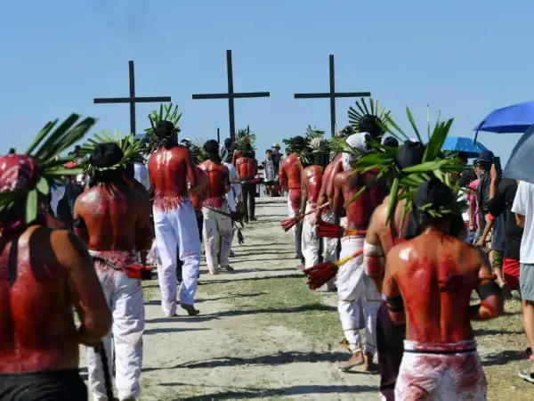 Hombres con coronas de hojas y espaldas ensangrentadas caminan hacia cruces negras, parte de una procesión de **Semana Santa Filipinas**.