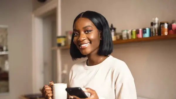 Lächelnde Frau mit Kaffee und Handy. Perfekt für die Darstellung von Teilzeit-Arbeit und dem Zeitaufwand, den sie mit sich bringt.