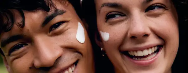 Coppia sorridente con crema sul viso, godendo dei benefici del vapore viso per una pelle radiosa.