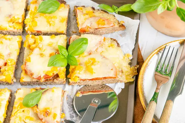 Herzhafte hackfleischpizza vom blech, Landfrauen-Art, mit Tomaten und Käse überbacken, garniert mit frischem Basilikum.
