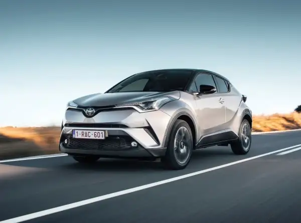 Srebrna Toyota C-HR 2023 pędzi po pustej drodze, z zachodzącym słońcem w tle.
