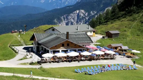 Die Hochalm Garmisch, ein beliebter Rastplatz mit vielen Gästen unter Sonnenschirmen, liegt malerisch vor einer beeindruckenden Bergkulisse.