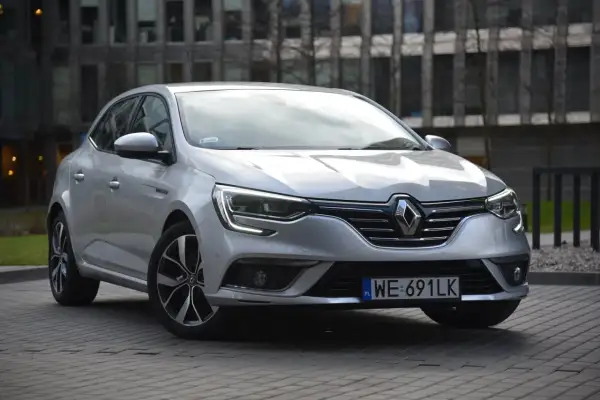 Srebrny Renault Megane 4 z nowoczesnymi żarówkami z przodu, zaparkowany przed budynkiem.