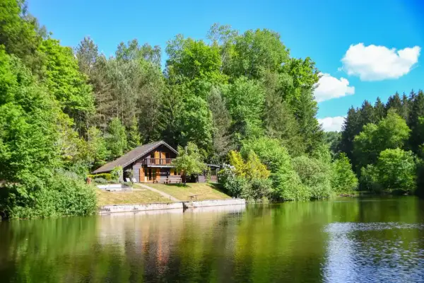 Charmant chalet en bois au bord d'un étang de pêche privé en Alsace, entouré de verdure luxuriante.