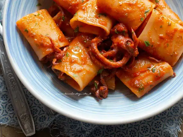 Paccheri con sugo di calamari, un piatto di mare saporito e colorato, con tentacoli che spuntano dalla pasta.