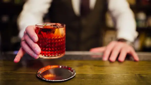 Ein Barkeeper reicht einen roten Cocktail mit Eis und Garnitur. Perfekt, um cocktail mixen lernen.