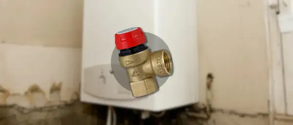 Gros plan sur un montage soupape de sécurité chaudière en laiton avec un capuchon rouge, installé sur une chaudière blanche.
