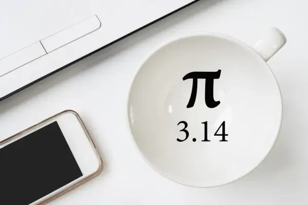 Biały kubek z symbolem π i liczbą 3.14, obok smartfon i fragment laptopa.