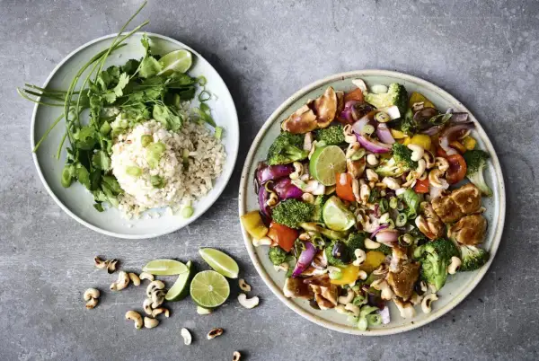 Två tallrikar med mat: en med ris, koriander och lime, den andra med kyckling, grönsaker och cashewnötter. Perfekt för nyttiga recept!