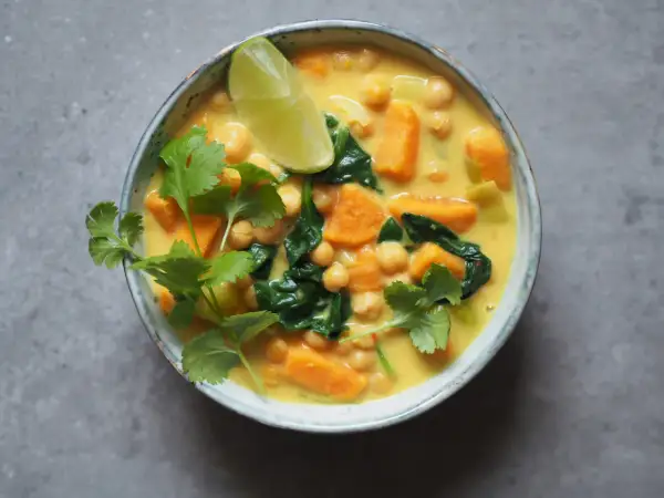 Aksamitne curry z ciecierzycy z kawałkami batata i szpinaku, ozdobione świeżą kolendrą i ćwiartką limonki.
