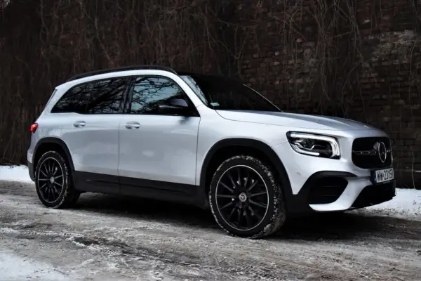 Srebrny Mercedes GLB 200 na zimowej drodze, z czarnymi felgami i przy ceglanym murze.