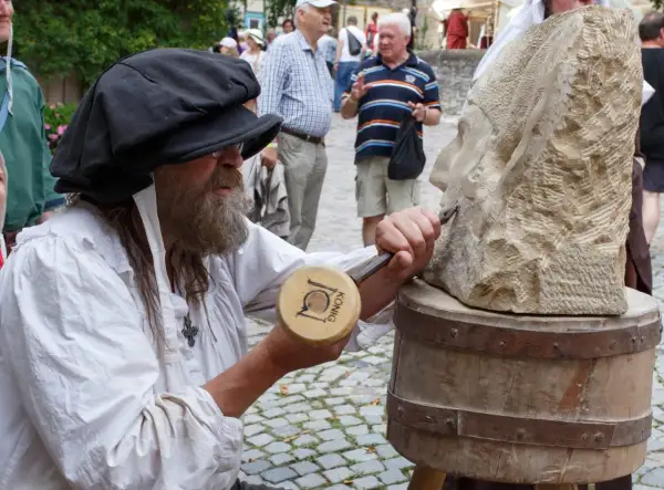 Steinmetz bei der Arbeit am Bad Wimpfen Zunftmarkt. Ein Mann mit Bart und schwarzer Kappe meißelt an einer Steinskulptur.