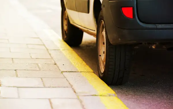 Un coche aparcado junto a una acera con marcas viales amarillas. El significado de estas marcas viales amarillas indica prohibición de estacionar.
