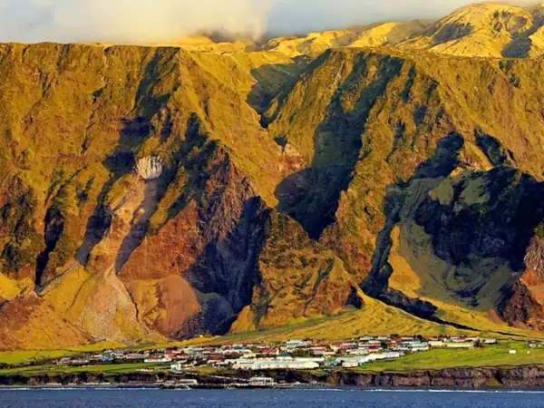 Un pueblo en Tristan de Acuña se asienta al pie de imponentes montañas cubiertas de hierba, bañadas por la luz dorada del atardecer.