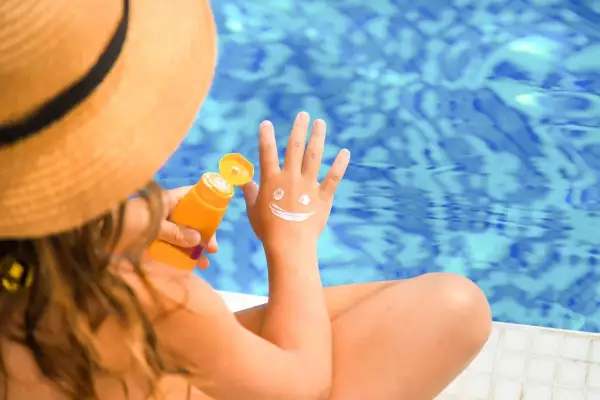 Kind mit Sonnenhut und LSF 50 Sonnencreme, die ein lachendes Gesicht auf die Hand malt.