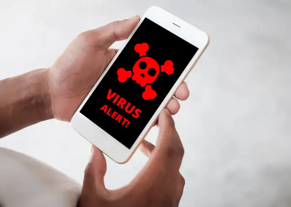 Dłonie trzymające smartfon z czerwonym symbolem czaszki i napisami "VIRUS ALERT!".