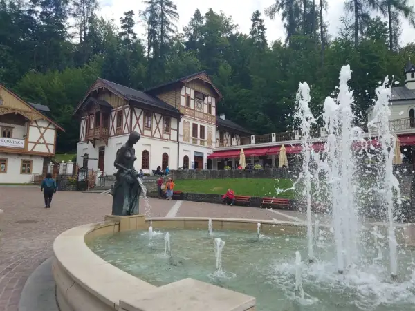 Fontanna i rzeźba w centrum, z pięknymi budynkami w tle. To jedne z wielu atrakcji Szczawnicy.