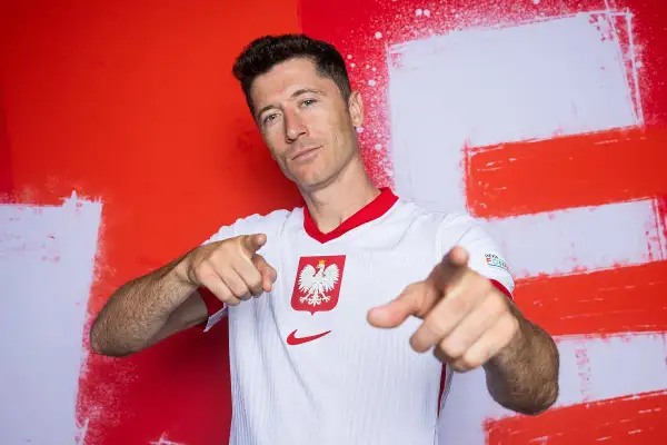 Robert Lewandowski, piłkarz roku uefa, w koszulce reprezentacji Polski, wskazuje palcami w stronę widza.