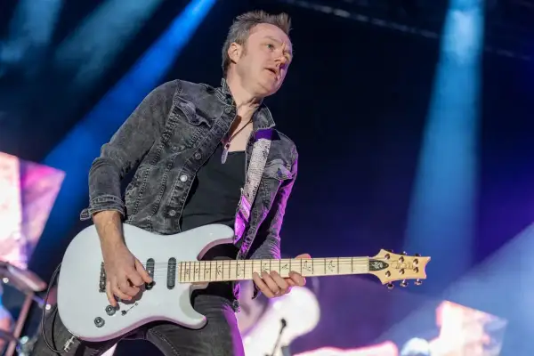 Chitarrista dei Deep Purple, con giacca di jeans scuro e chitarra bianca, sul palco illuminato da luci blu.
