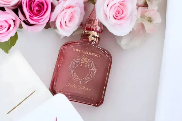 Różowe róże otaczają flakonik perfum Charlotte Tilbury Love Frequency.