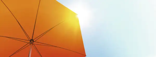 Ein orangefarbener Sonnenschirm schützt vor der Sonne. Seine Struktur ist sichtbar, während Sonnenstrahlen durchscheinen. Diethylhexyl Butamido Triazone schützt die Haut.