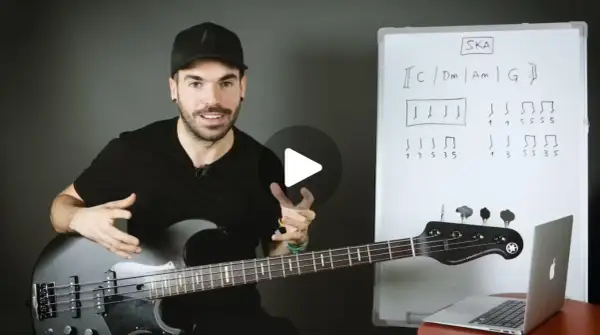Hombre con bajo explica qué es el ska con un diagrama musical en una pizarra.