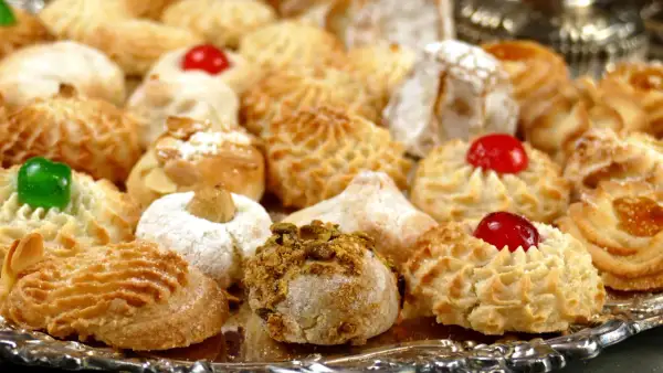 Vassoio pieno di biscotti alle mandorle, alcuni decorati con ciliegie rosse, mandorle e pistacchi.