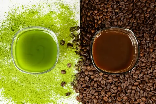Zielony napój matcha obok ciemnej kawy, otoczone proszkiem matcha i ziarnami kawy. Wybór na poranek: matcha zamiast kawy?