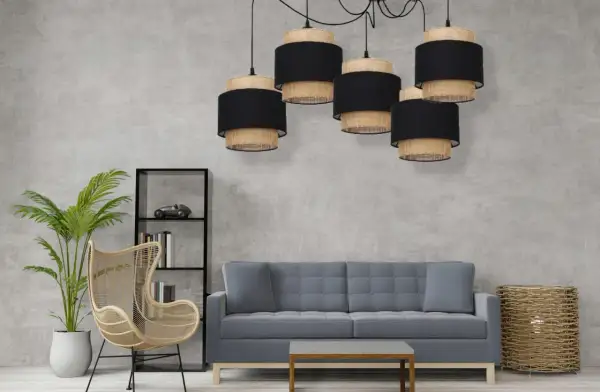 Pięcioramienna lampa pająk boho z abażurami z plecionki i czarnego materiału nad szarą sofą.