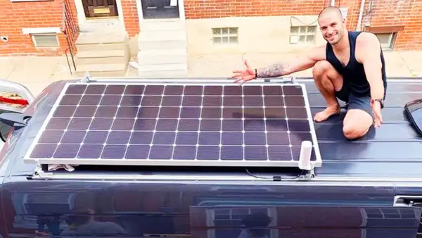 Hombre muestra cómo conectar dos placas solares en el techo de una furgoneta.