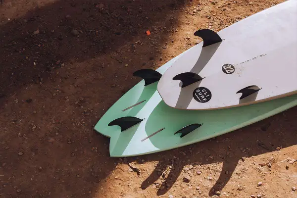 Zwei Surfbretter mit Finnen liegen auf sandigem Boden. Perfekt für die packliste surfcamp.