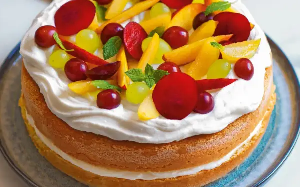 Torta compleanno pan di spagna con panna montata e frutta fresca: pesche, uva rossa e bianca, prugne e foglioline di menta.