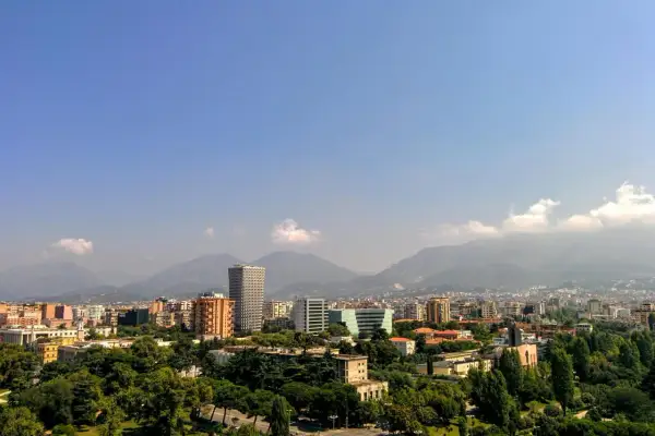 Widok na miasto z górami w tle. Widać nowoczesne budynki i zieleń. Idealne miejsce na **Albania roaming** i odkrywanie krajobrazów.