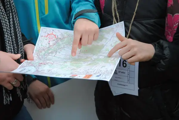 Dłonie wskazują trasę na mapie podczas biegu na orientację.